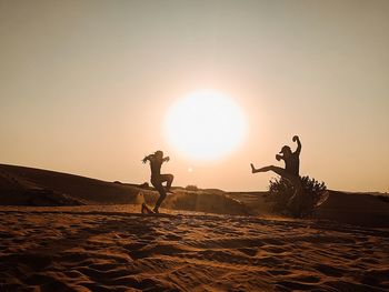 Silhouette people jumping on desert against sky during sunset