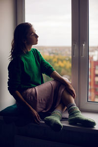 Woman sitting on the window in the green sweater in the fall