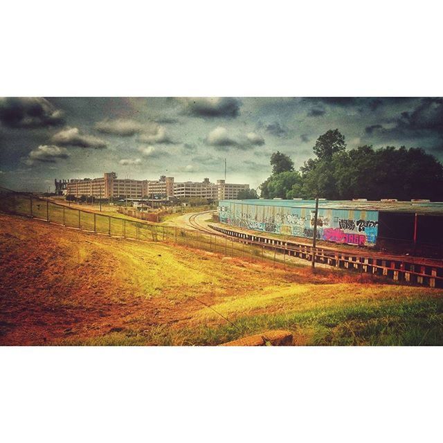 sky, transportation, transfer print, auto post production filter, railroad track, rail transportation, architecture, building exterior, built structure, cloud - sky, train - vehicle, public transportation, cloudy, overcast, field, grass, day, road, outdoors, no people