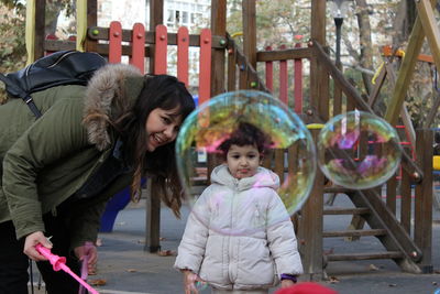 Cute girl seen through bubble standing with mother outdoors