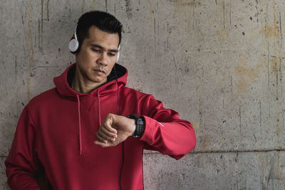 Man checking time while listening to music against wall