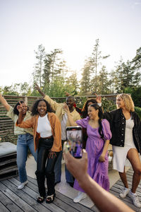 Hand of man filming male and female friends dancing together in back yard