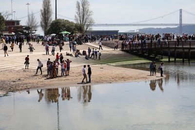 People at tagus riverbank against 25 de abril bridge
