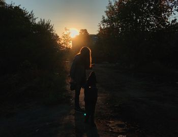 Rear view of woman standing on land against sky during sunset