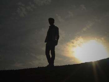 Silhouette man standing on field against sky at sunset