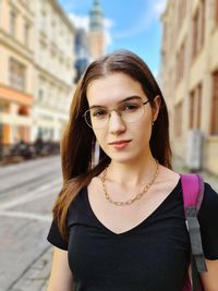 Portrait of young woman standing against building in city