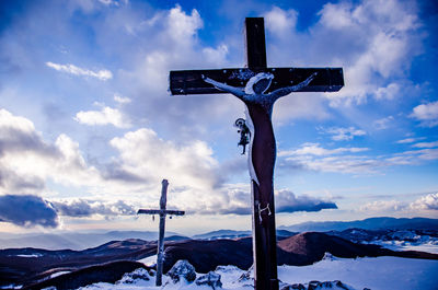Low angle view of cross on snow covered mountain against sky