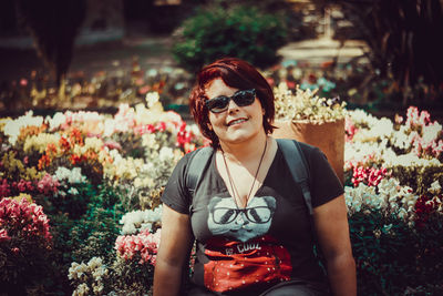 Portrait of smiling woman wearing sunglasses sitting against flowers