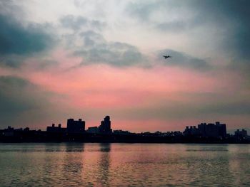 Silhouette city by sea against sky during sunset