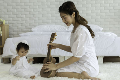 Full length of mother holding ukulele while sitting with daughter at home