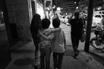 Rear view of friends standing on sidewalk in city at night