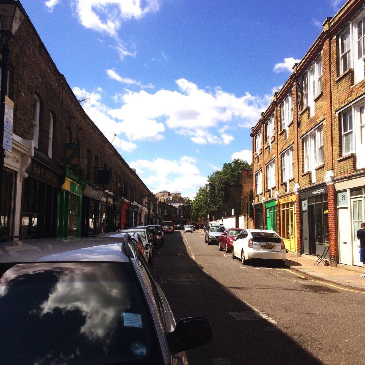 building exterior, architecture, transportation, built structure, car, land vehicle, street, mode of transport, sky, road, city, the way forward, sunlight, city street, building, residential building, cloud, incidental people, diminishing perspective, parking