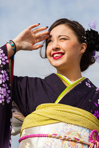 Low angle view of smiling woman shielding eyes while wearing kimono