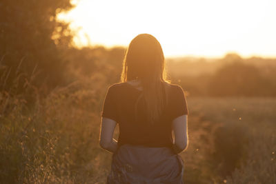 Woman standing on field against sky during sunset