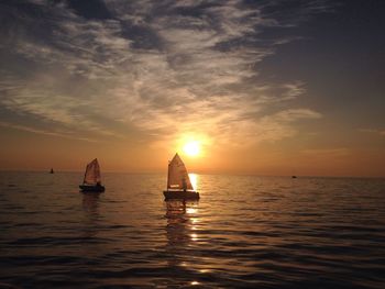 Sailboats sailing in sea against sky during sunset