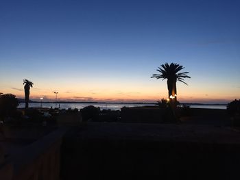 Silhouette palm trees by sea against clear sky during sunset