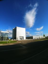 Road by buildings against blue sky