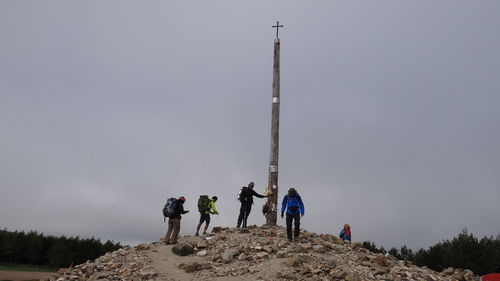 Low angle view of people standing on mountain against sky