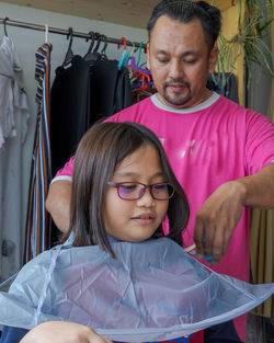 Asian young girl wearing glasses getting haircut at home from the father.