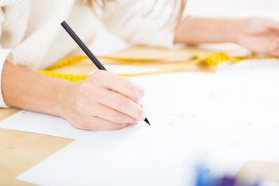 Midsection of woman writing on paper at office desk