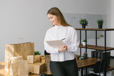 A cute girl in the office smiles and makes notes in a notebook next to eco packages on the table