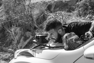 Side view of young man sitting in car to taje a pic polaroid