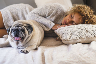 Portrait of young woman with dog lying on bed at home