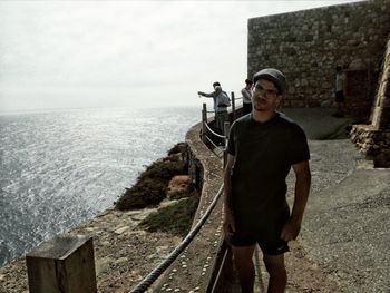 Portrait of mature man standing on cliff by sea against sky during sunny day