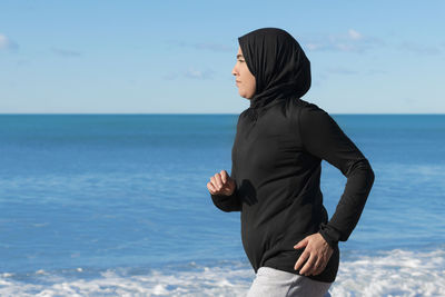 Side view of woman standing at beach against sky