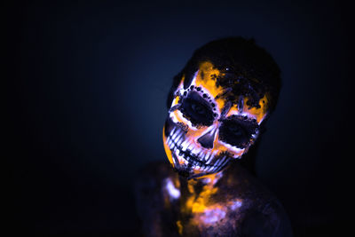 Close-up portrait of woman wearing illuminated spooky mask against black background