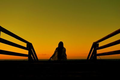 Rear view of silhouette woman standing by railing against sky during sunset