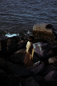 Rear view of woman sitting on rock by sea