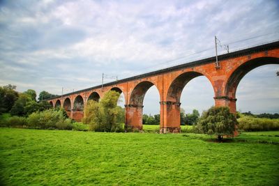 Arch bridge over field against sky