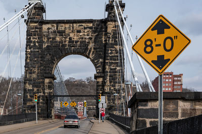 Road sign on bridge against sky in city