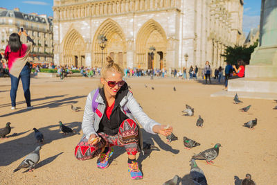 Smiling woman feeding pigeons in city 