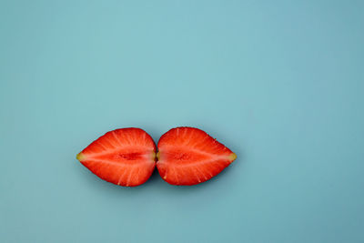 Juicy fresh strawberries, split into two halves on a blue background.