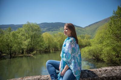 Woman sitting by lake against trees