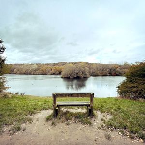 Empty bench by lake against sky