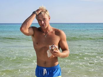 Shirtless man with arms outstretched at beach