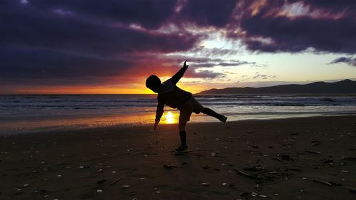 Silhouette boy playing at beach during sunset