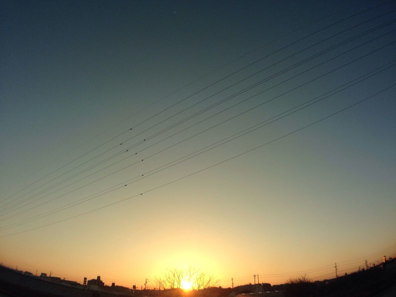 sunset, silhouette, clear sky, sun, copy space, low angle view, beauty in nature, orange color, nature, sky, sunlight, scenics, tranquility, tranquil scene, outdoors, dusk, outline, power line, blue, no people