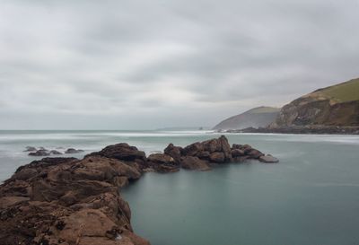 Scenic view of rocky mountains and sea against cloudy sky