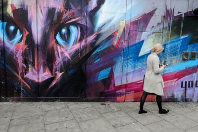 Full length of woman by graffiti wall on sidewalk