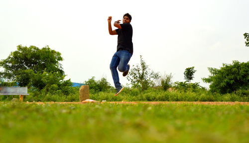 Low angle view of young woman jumping on grass against sky