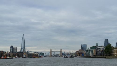 Thames river amidst buildings against cloudy sky