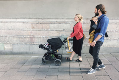 Full length of mid adult parents with baby boy and carriage walking on sidewalk