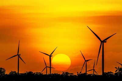 Silhouette wind turbines on field against sky during sunset