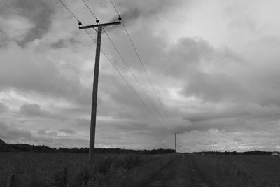 Road passing through field against cloudy sky