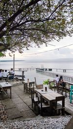 People sitting on bench by sea against sky