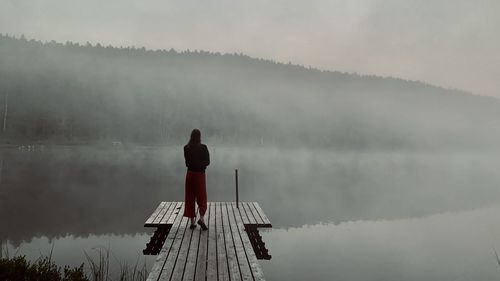 Rear view of girl standing on lake against sky